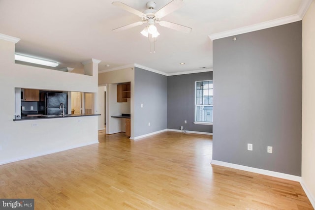 unfurnished living room with ceiling fan, a sink, light wood-style flooring, baseboards, and ornamental molding