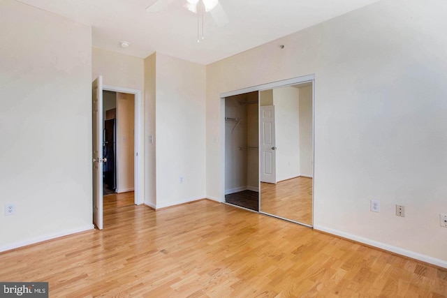 unfurnished bedroom featuring light wood-style flooring, freestanding refrigerator, a ceiling fan, baseboards, and a closet