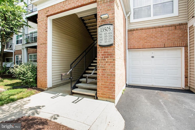 property entrance featuring brick siding, an attached garage, and driveway