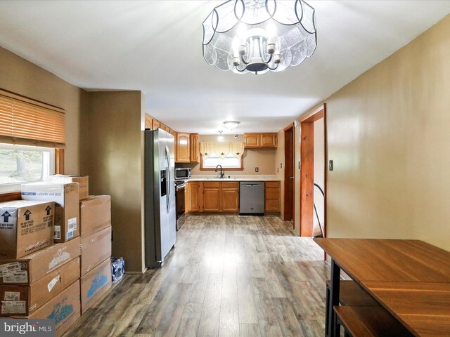 kitchen with light countertops, a sink, light wood finished floors, a notable chandelier, and stainless steel appliances