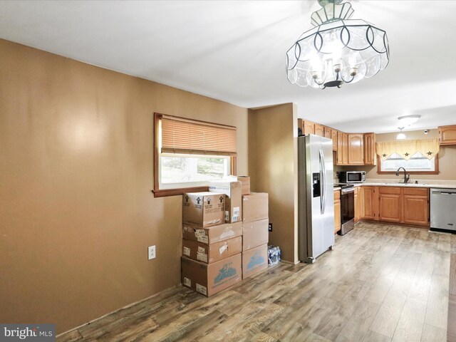 kitchen with light wood-type flooring, a sink, light countertops, an inviting chandelier, and stainless steel appliances