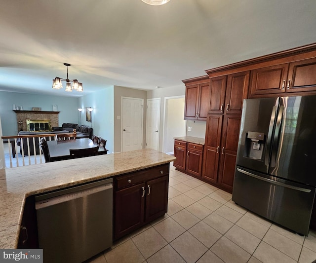 kitchen with appliances with stainless steel finishes, light stone countertops, light tile patterned floors, a chandelier, and a glass covered fireplace