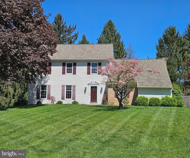 colonial inspired home with roof with shingles, a chimney, and a front yard