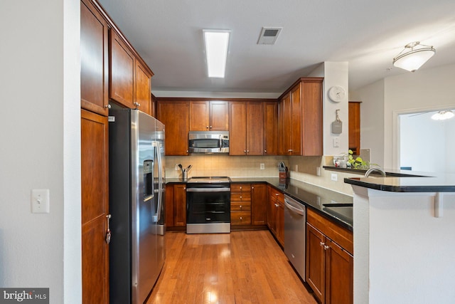 kitchen featuring visible vents, dark countertops, light wood-type flooring, appliances with stainless steel finishes, and backsplash