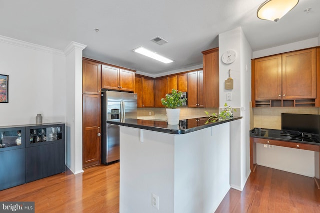 kitchen featuring dark countertops, stainless steel fridge, light wood-style floors, brown cabinetry, and backsplash