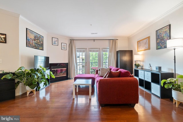 living area featuring visible vents, ornamental molding, a glass covered fireplace, and wood finished floors