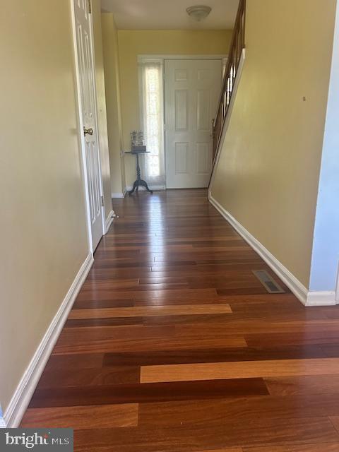 hall featuring baseboards, wood-type flooring, and visible vents