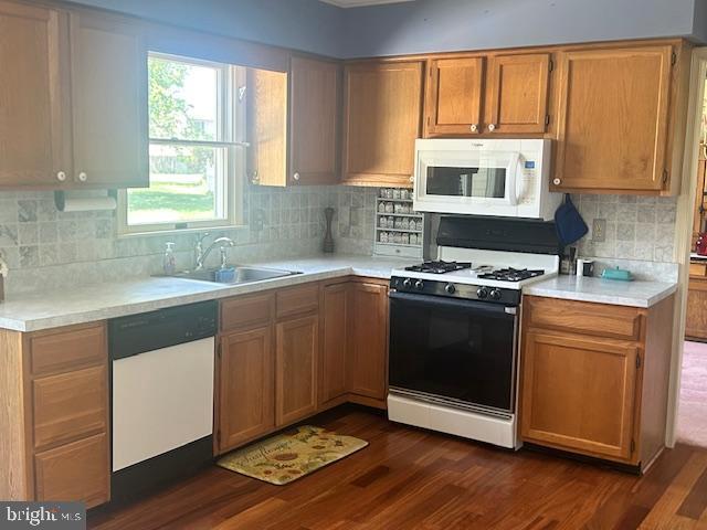 kitchen featuring backsplash, a sink, light countertops, white appliances, and dark wood-type flooring