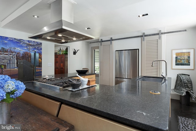 kitchen with high end refrigerator, island range hood, a sink, a barn door, and dark stone counters