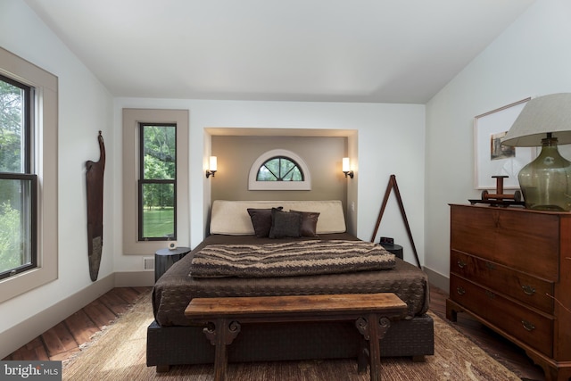 bedroom with multiple windows, wood finished floors, and baseboards
