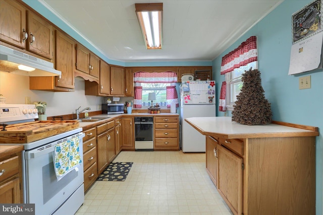 kitchen with white appliances, light countertops, under cabinet range hood, brown cabinets, and a sink