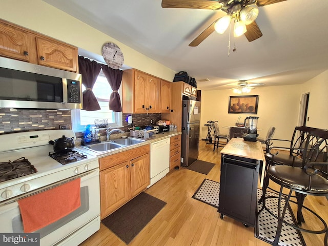 kitchen featuring a sink, light wood finished floors, stainless steel appliances, a ceiling fan, and decorative backsplash