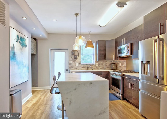kitchen with dark brown cabinetry, appliances with stainless steel finishes, a sink, a center island, and backsplash