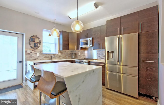 kitchen featuring dark brown cabinets, light wood finished floors, a center island, stainless steel appliances, and backsplash