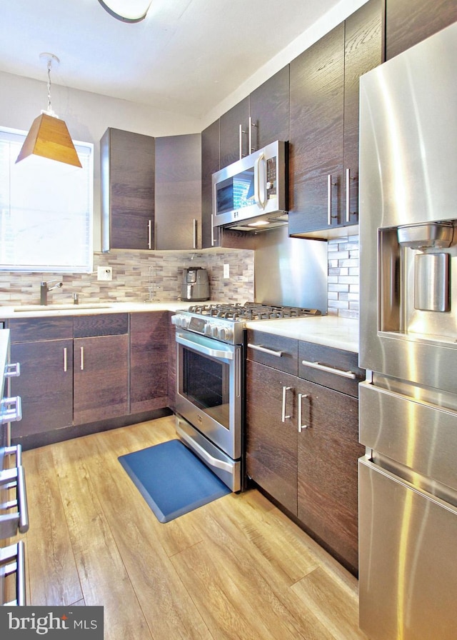 kitchen with light wood-style floors, light countertops, tasteful backsplash, a sink, and appliances with stainless steel finishes