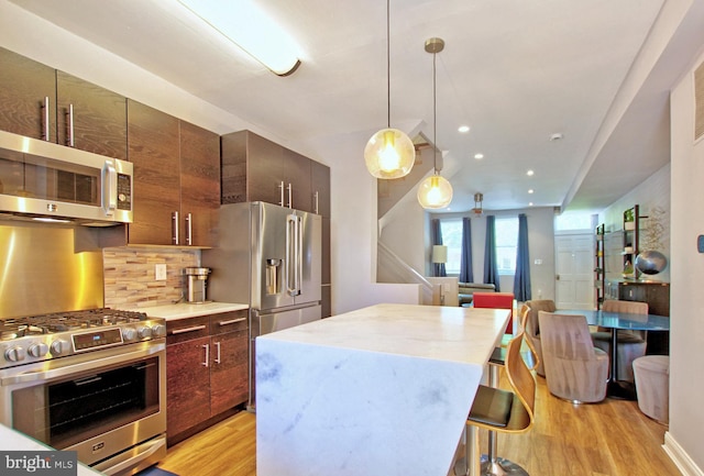 kitchen featuring light wood-style floors, a kitchen breakfast bar, a center island, tasteful backsplash, and appliances with stainless steel finishes