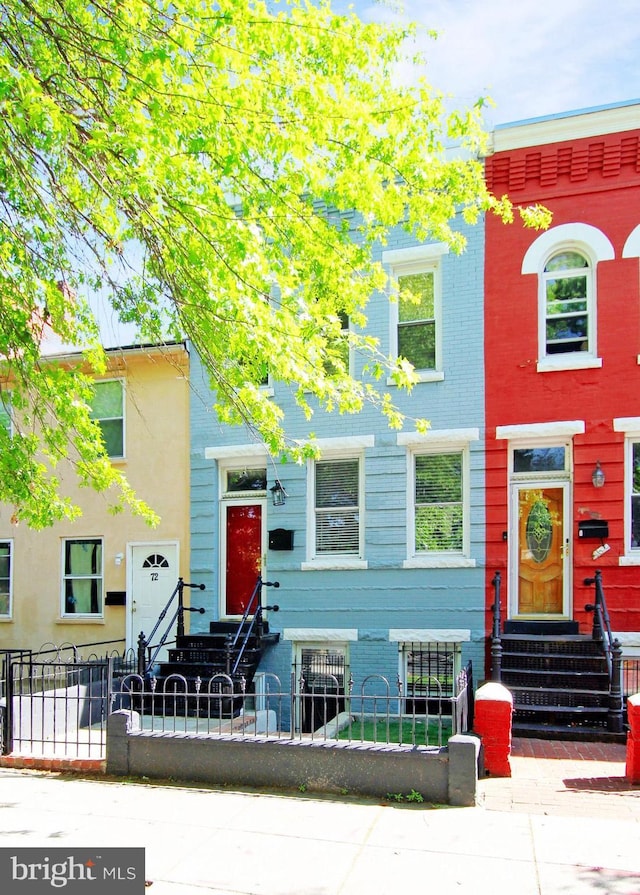 townhome / multi-family property with brick siding, a fenced front yard, and entry steps