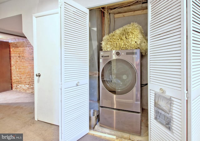 clothes washing area with laundry area, washer / dryer, carpet, and brick wall