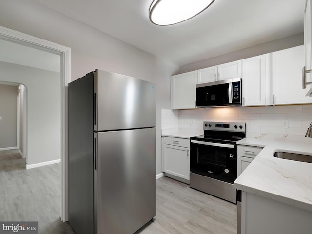 kitchen with appliances with stainless steel finishes, decorative backsplash, a sink, and light wood-type flooring