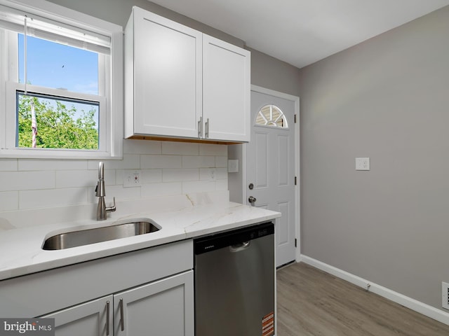 kitchen featuring stainless steel dishwasher, baseboards, tasteful backsplash, a sink, and light wood-style flooring
