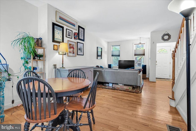 dining space with light wood-type flooring, stairs, baseboards, and visible vents