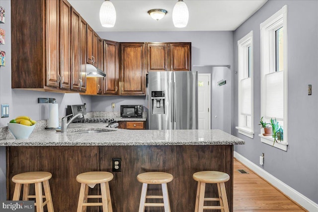 kitchen featuring light stone counters, a peninsula, appliances with stainless steel finishes, and under cabinet range hood