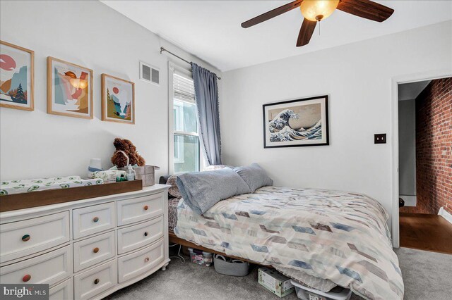 carpeted bedroom with visible vents, ceiling fan, and brick wall