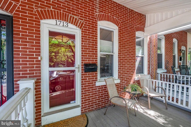 view of exterior entry with brick siding and a porch
