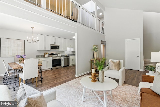 living area with wood finished floors, a chandelier, baseboards, a high ceiling, and recessed lighting