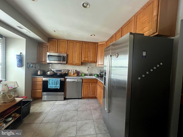 kitchen featuring brown cabinetry, appliances with stainless steel finishes, a sink, light countertops, and recessed lighting