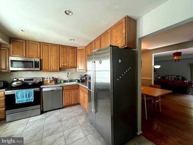 kitchen with brown cabinets, a sink, light countertops, stainless steel appliances, and recessed lighting