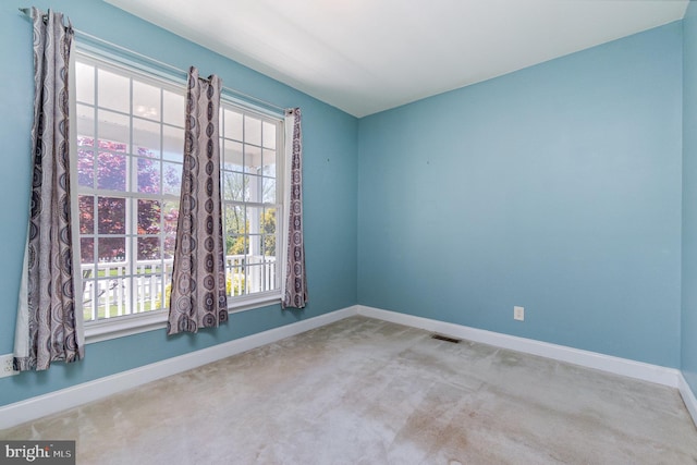 carpeted empty room featuring a healthy amount of sunlight, baseboards, and visible vents