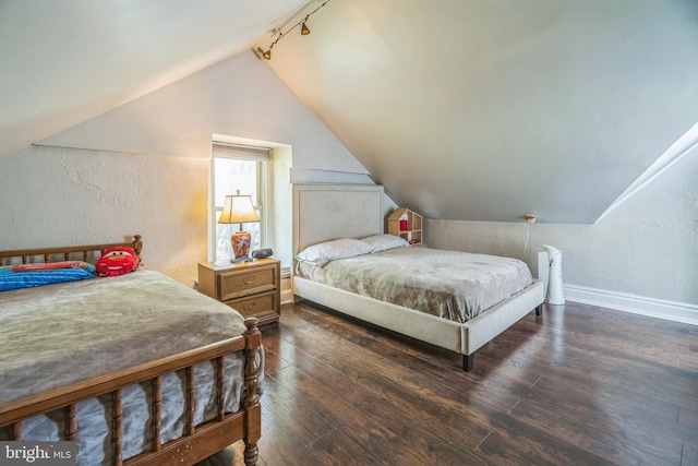 bedroom with track lighting, baseboards, dark wood-style floors, lofted ceiling, and a textured wall