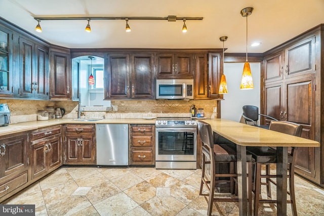 kitchen with decorative backsplash, a sink, light countertops, rail lighting, and appliances with stainless steel finishes
