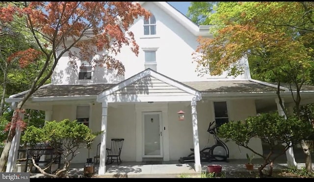 exterior space featuring a porch, roof with shingles, and stucco siding
