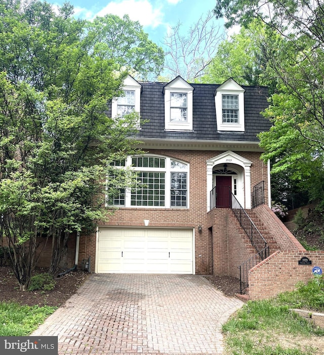 cape cod-style house featuring an attached garage, decorative driveway, and brick siding