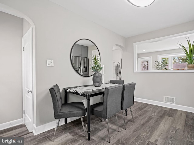 dining area with arched walkways, baseboards, visible vents, and dark wood-style floors