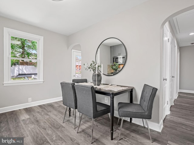 dining space featuring baseboards, attic access, arched walkways, and wood finished floors