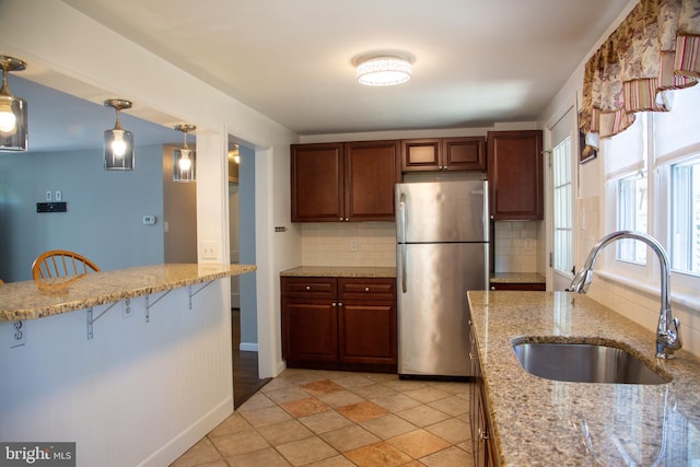 kitchen featuring freestanding refrigerator, a breakfast bar area, light stone counters, a sink, and backsplash