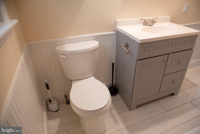half bath featuring a wainscoted wall, tile patterned floors, vanity, and toilet