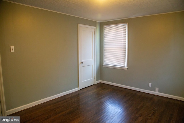 spare room with dark wood-type flooring, ornamental molding, and baseboards