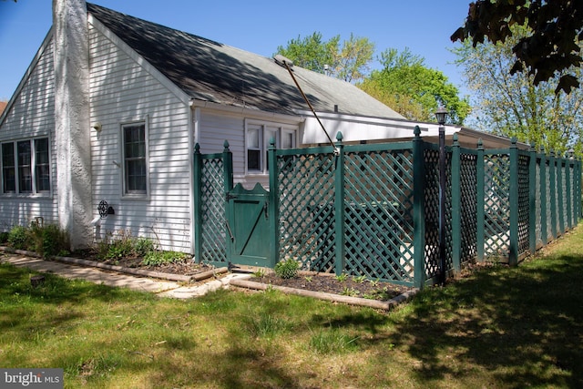 view of side of property featuring a lawn, a gate, a chimney, and a shingled roof