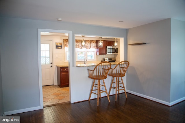 kitchen with a breakfast bar, baseboards, hardwood / wood-style flooring, tasteful backsplash, and appliances with stainless steel finishes