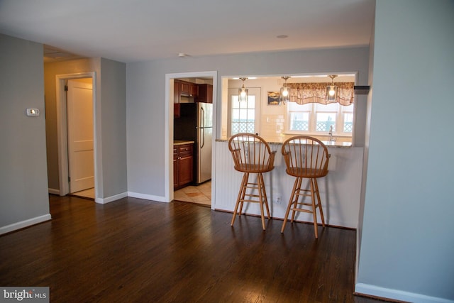 kitchen featuring freestanding refrigerator, a peninsula, wood finished floors, a breakfast bar area, and light stone counters