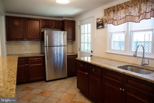kitchen featuring a sink, light stone counters, freestanding refrigerator, and backsplash
