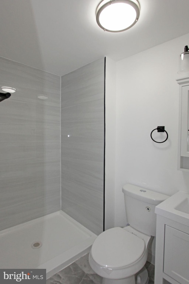 bathroom featuring vanity, a tile shower, and toilet