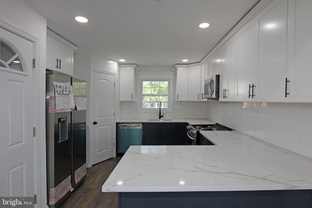 kitchen with a sink, stainless steel appliances, a peninsula, decorative backsplash, and dark wood-style floors