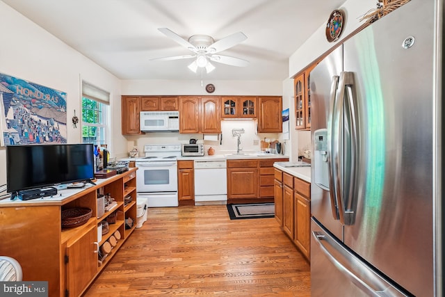 kitchen with a sink, brown cabinetry, ceiling fan, white appliances, and light countertops