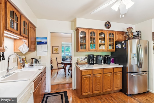 kitchen with glass insert cabinets, brown cabinetry, a sink, stainless steel fridge with ice dispenser, and light countertops