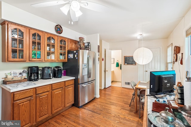 kitchen featuring ceiling fan, light countertops, brown cabinetry, and stainless steel refrigerator with ice dispenser